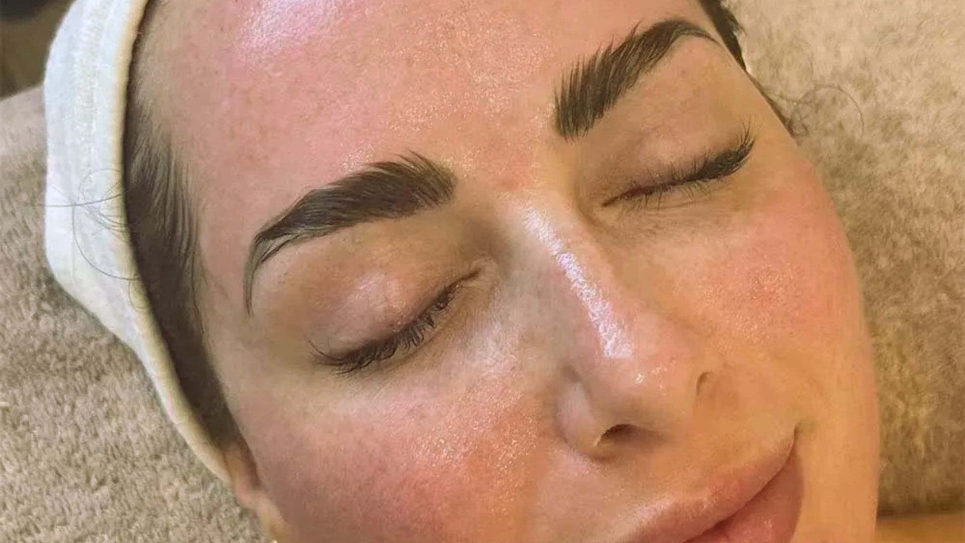 A woman receiving an eyebrow shaping treatment at a spa, sitting comfortably in a salon chair.