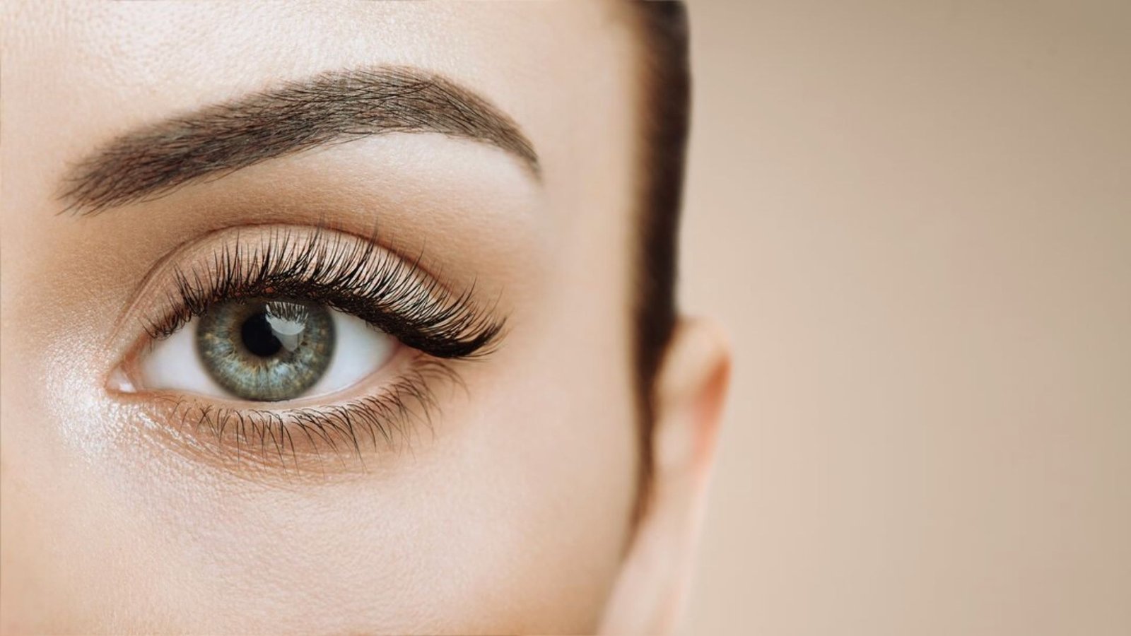 A close-up of a woman's eye showcasing long, elegant eyelashes against a soft background.
