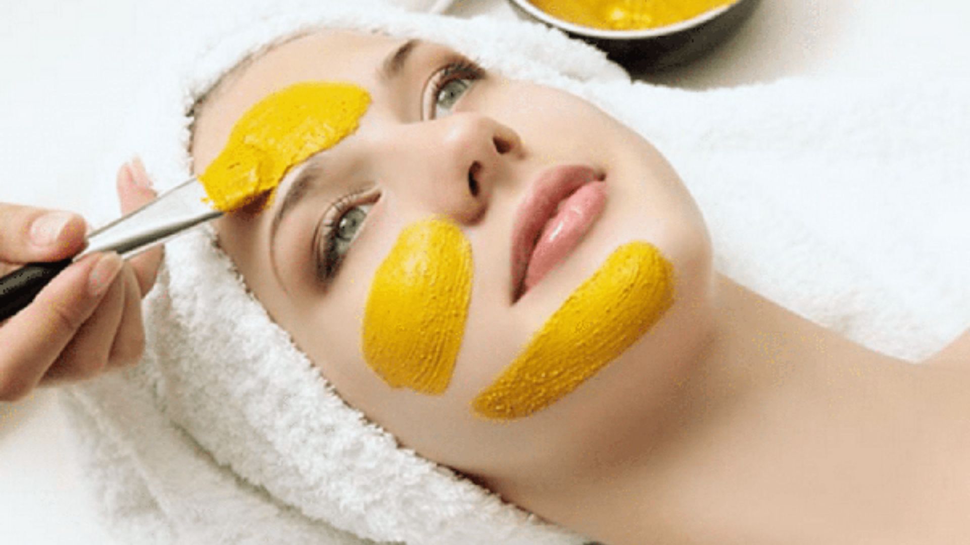  A woman receiving a facial treatment, wearing a bright yellow face mask, relaxing in a spa setting.