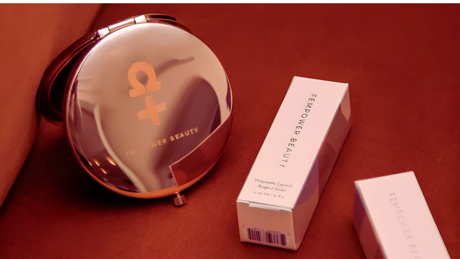 A compact mirror next to an open box of makeup, showcasing various cosmetic products inside