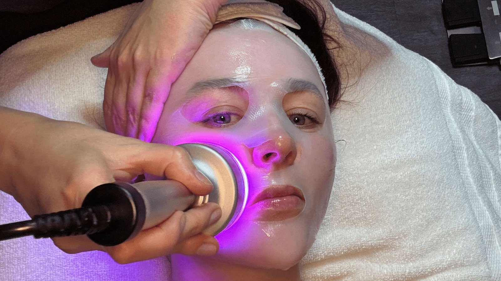 A woman receiving a facial treatment under a soothing purple light, enhancing her skincare experience.