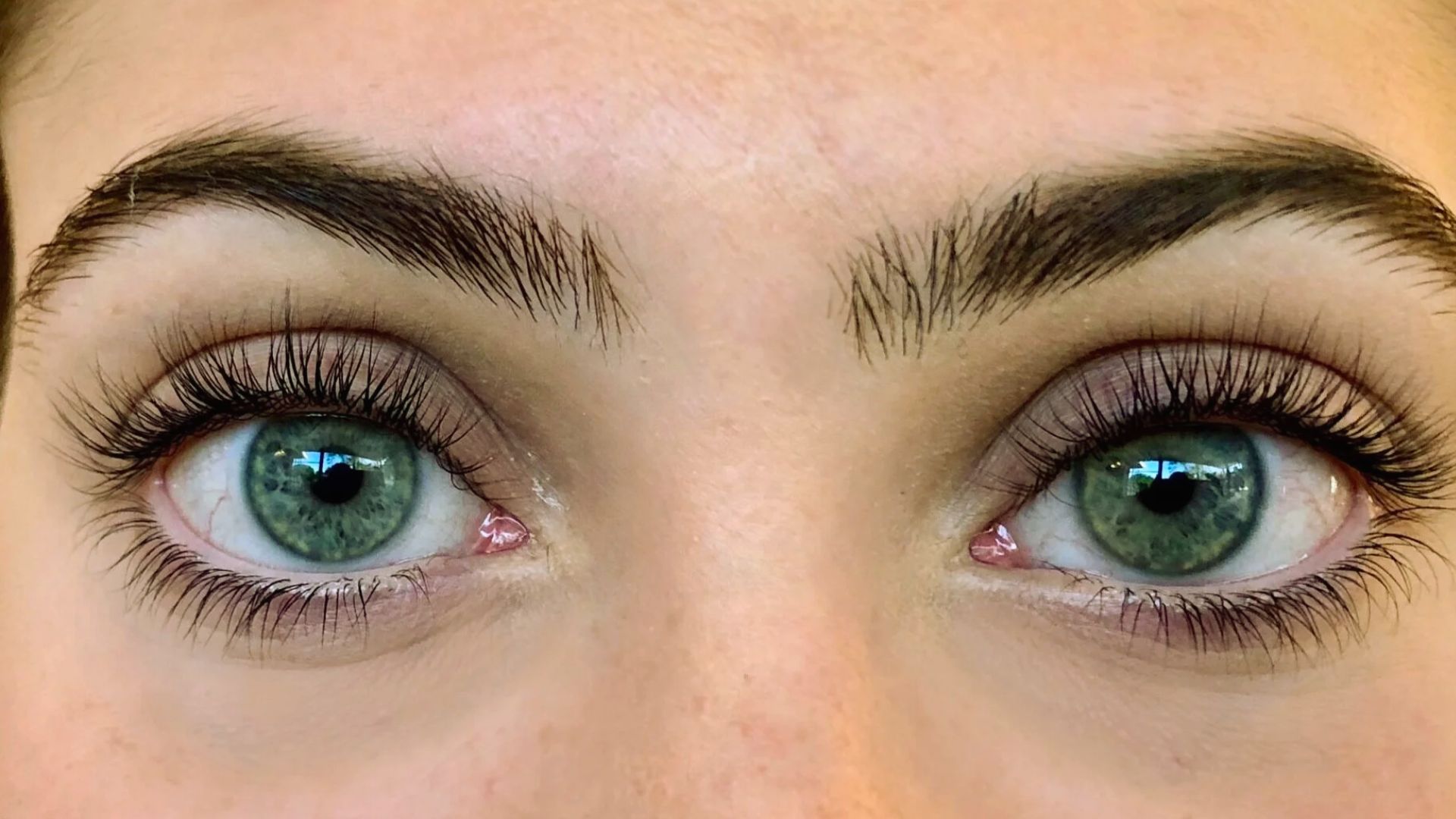 A woman with long eyelashes and vibrant green eyes smiles softly, showcasing her unique features.