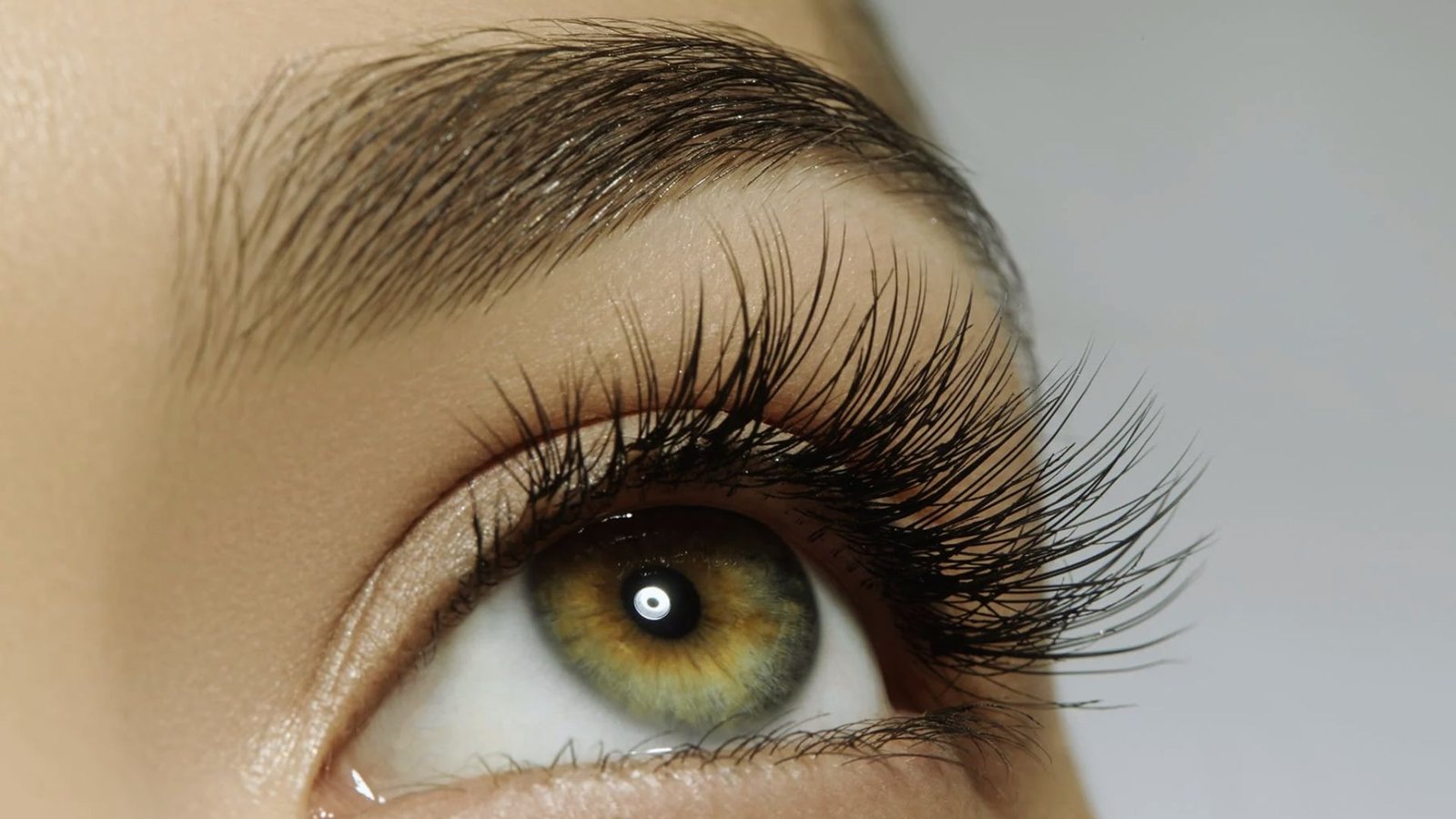 A close-up of a woman's eye showcasing long, elegant eyelashes against a soft background.