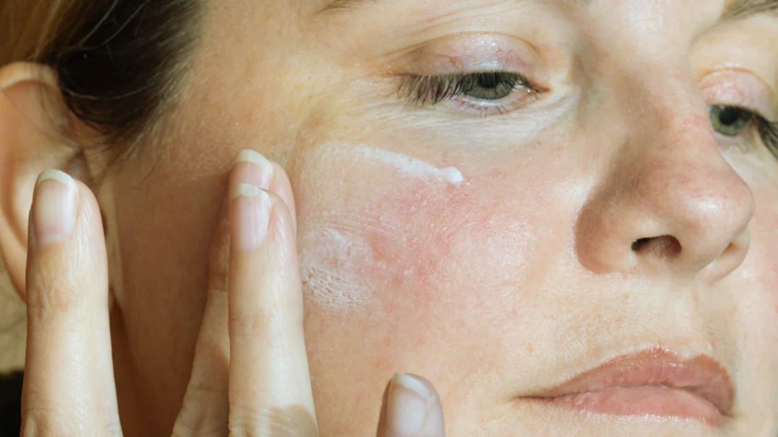 A woman with a white face and hand gently holding her face, conveying a sense of contemplation or introspection.