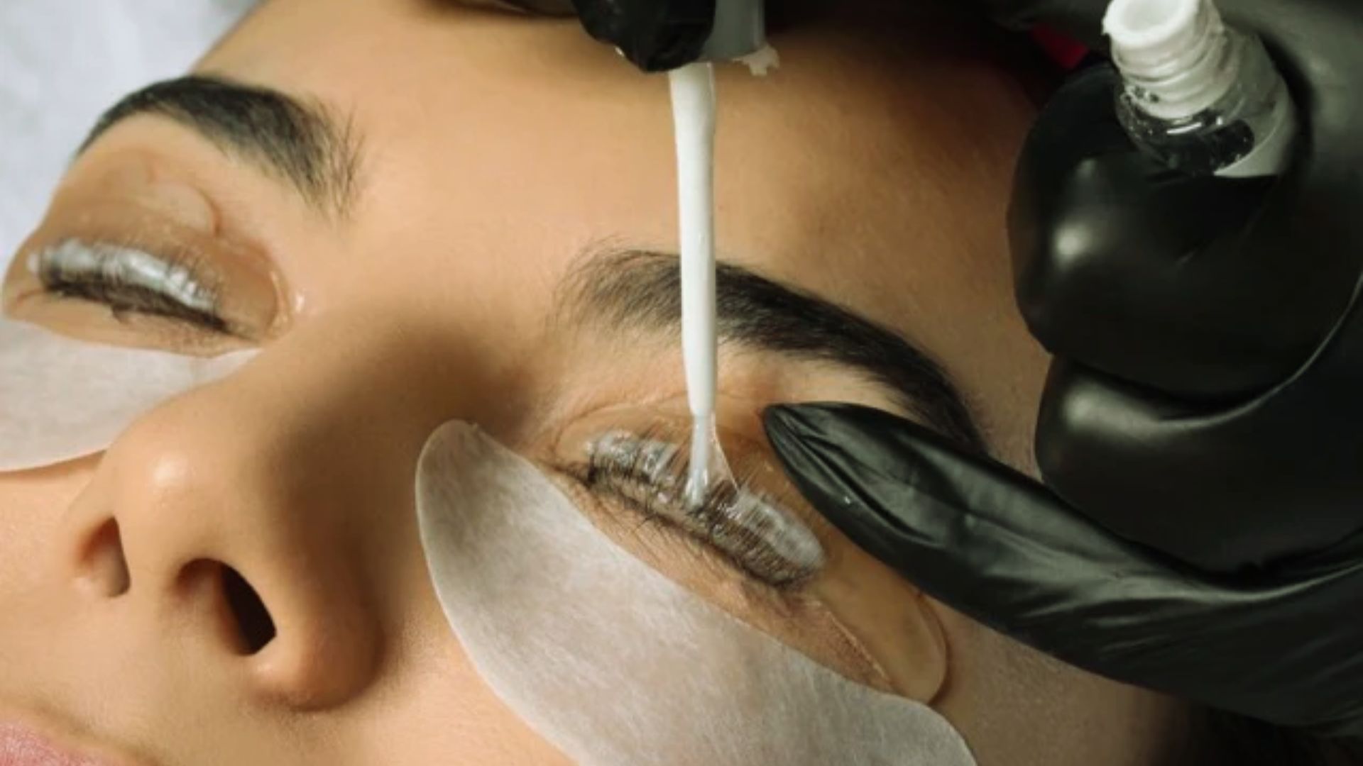  A woman receiving eyelash extensions using a machine in a beauty salon setting.