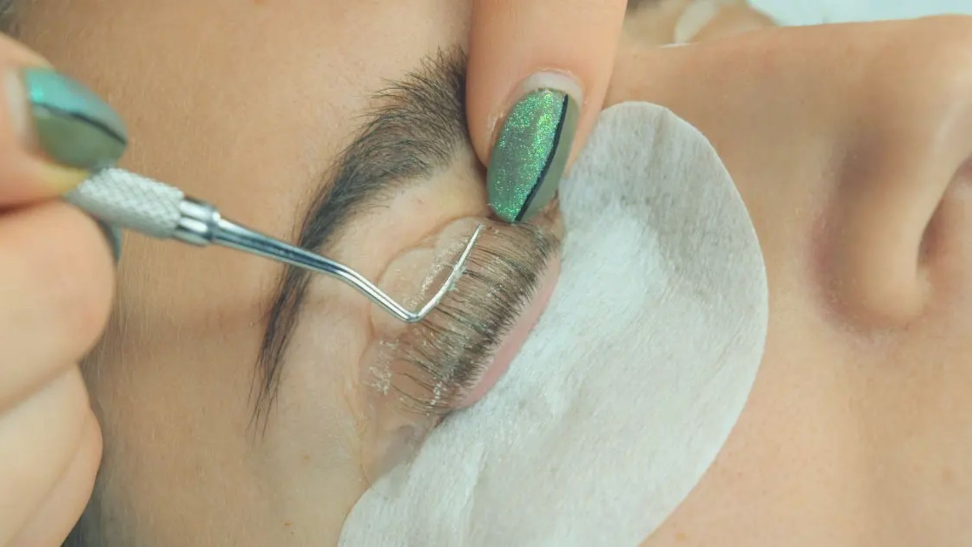 A woman is having her eyelashes enhanced by a beauty professional in a well-lit salon.