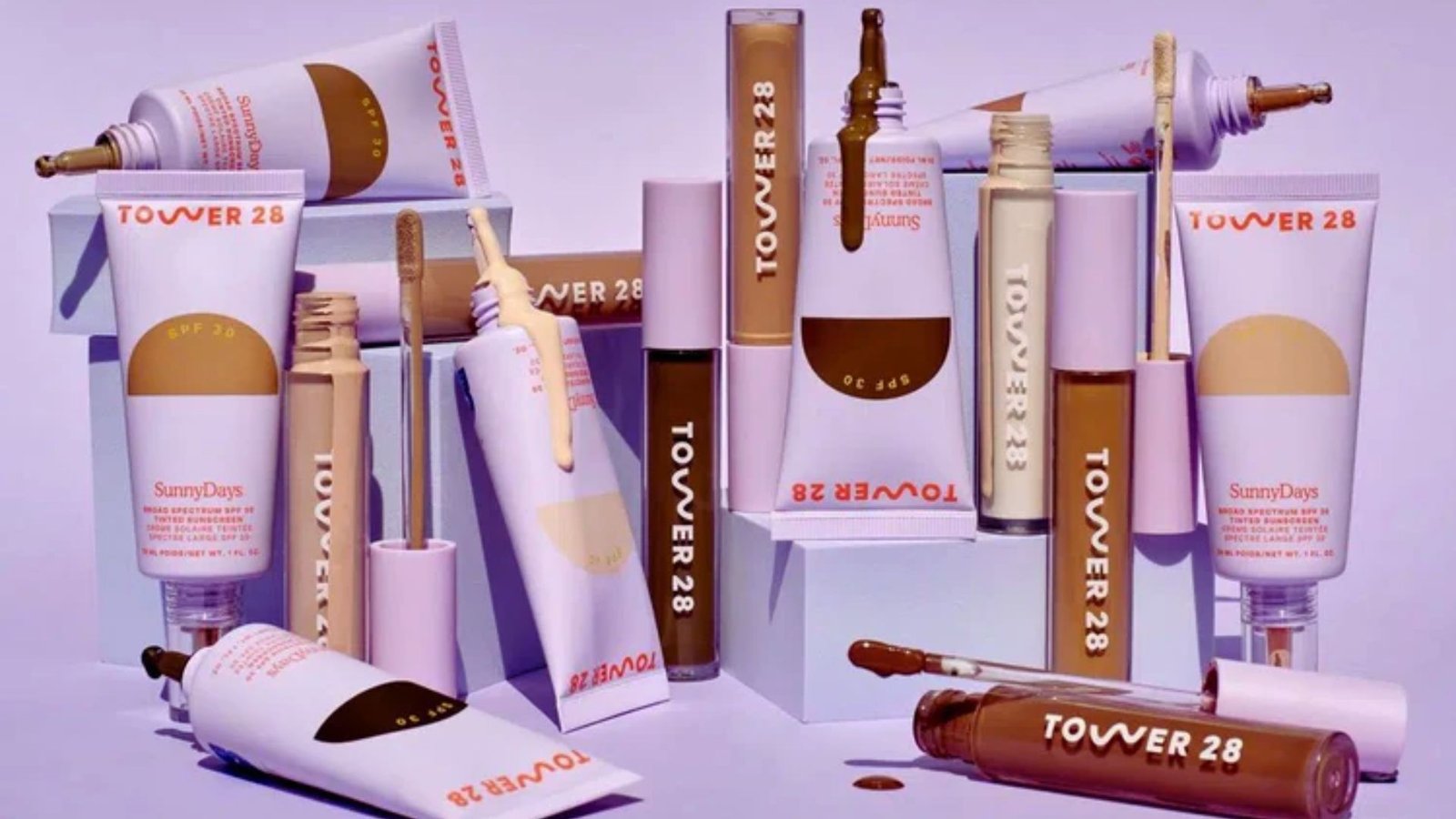 A collection of various makeup products displayed on a vibrant purple background.