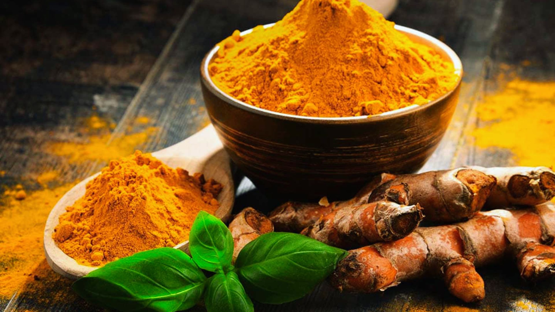 Fresh turmeric root beside a small bowl of vibrant yellow turmeric powder on a wooden surface.