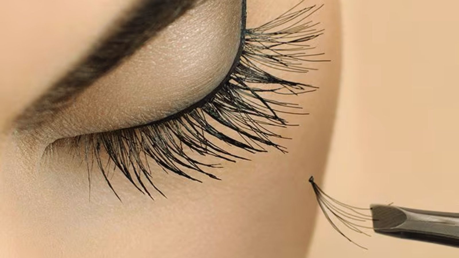 A close-up of a woman's eye with long eyelashes, featuring a makeup brush positioned nearby.