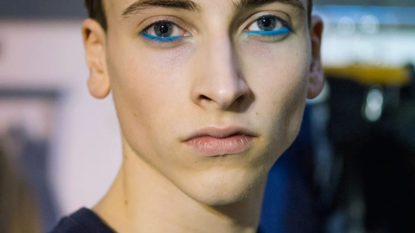 A young man with blue eyes wearing a black shirt, looking directly at the camera with a neutral expression.