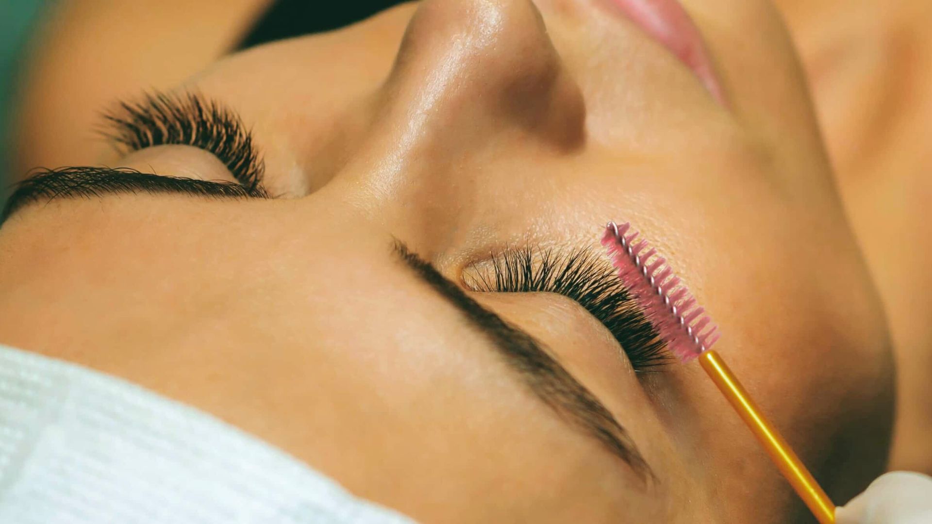 A woman having her eyelashes styled with a brush, focusing on enhancing their length and volume.
