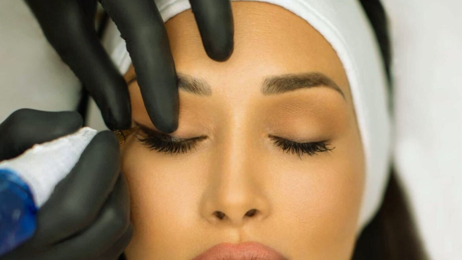 A woman receiving an eyebrow treatment using a machine in a beauty salon setting.