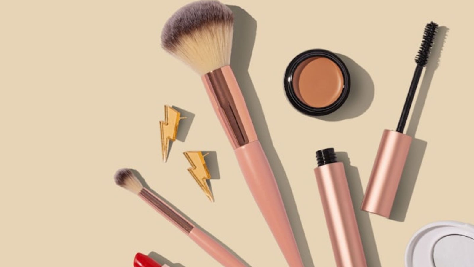 Various cosmetics including brushes, mascara, and lipstick displayed on a soft beige surface.