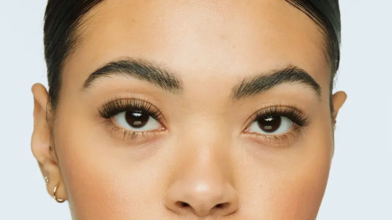 A woman with dark brown eyes and light brown lips, showcasing a natural and elegant makeup look.