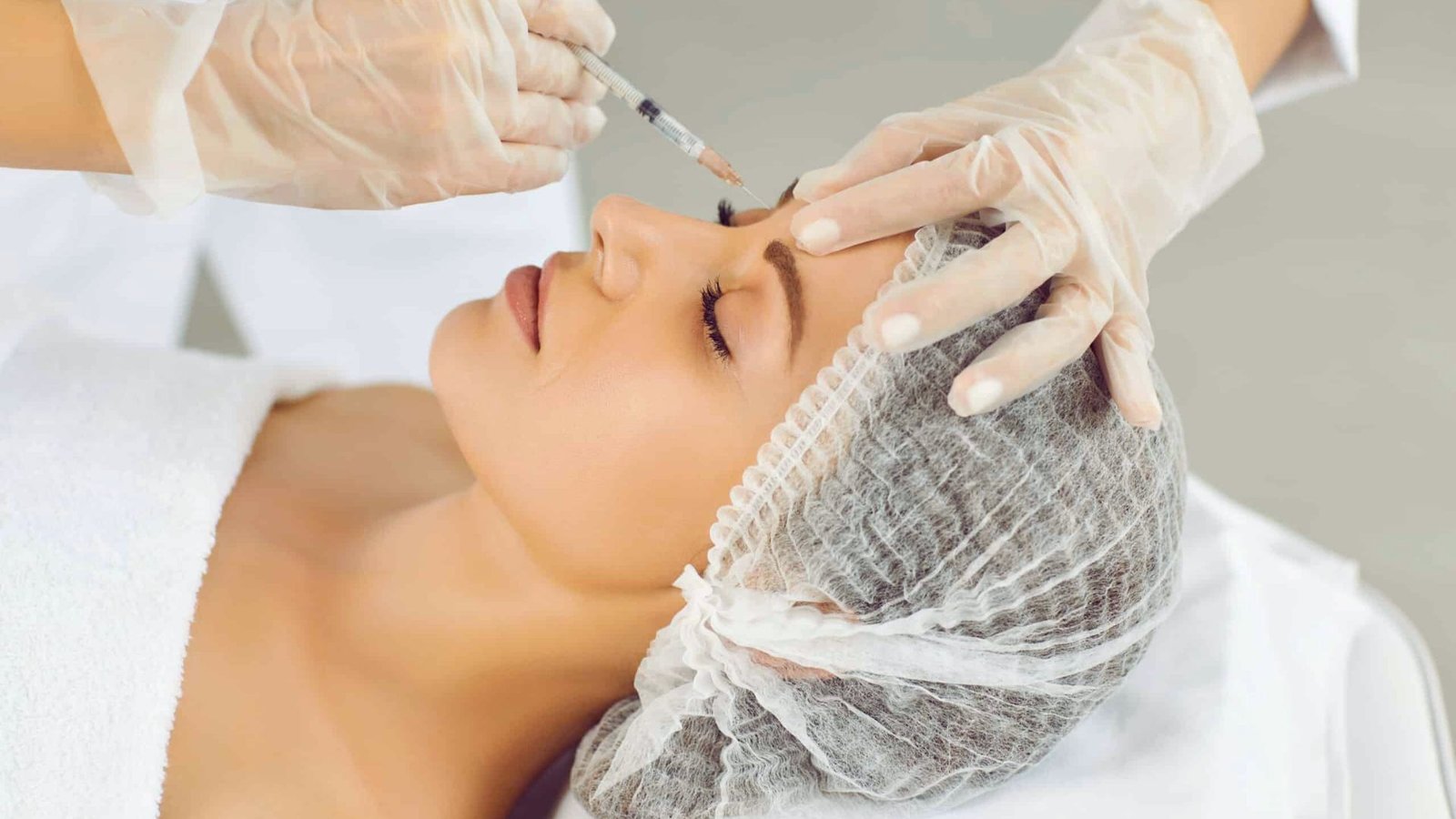 A woman receiving a facial treatment, relaxing on a spa bed with a serene expression and a therapist applying products.