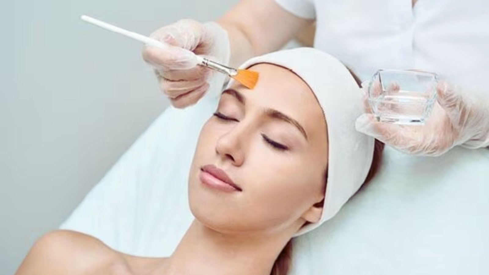 A woman receiving a facial treatment, relaxing on a spa bed with a serene expression and a therapist applying products.