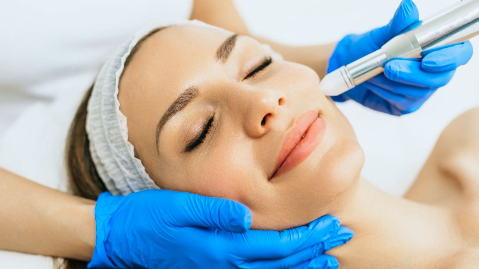 A woman receiving a facial treatment, relaxing on a spa bed with a serene expression and a therapist applying products.