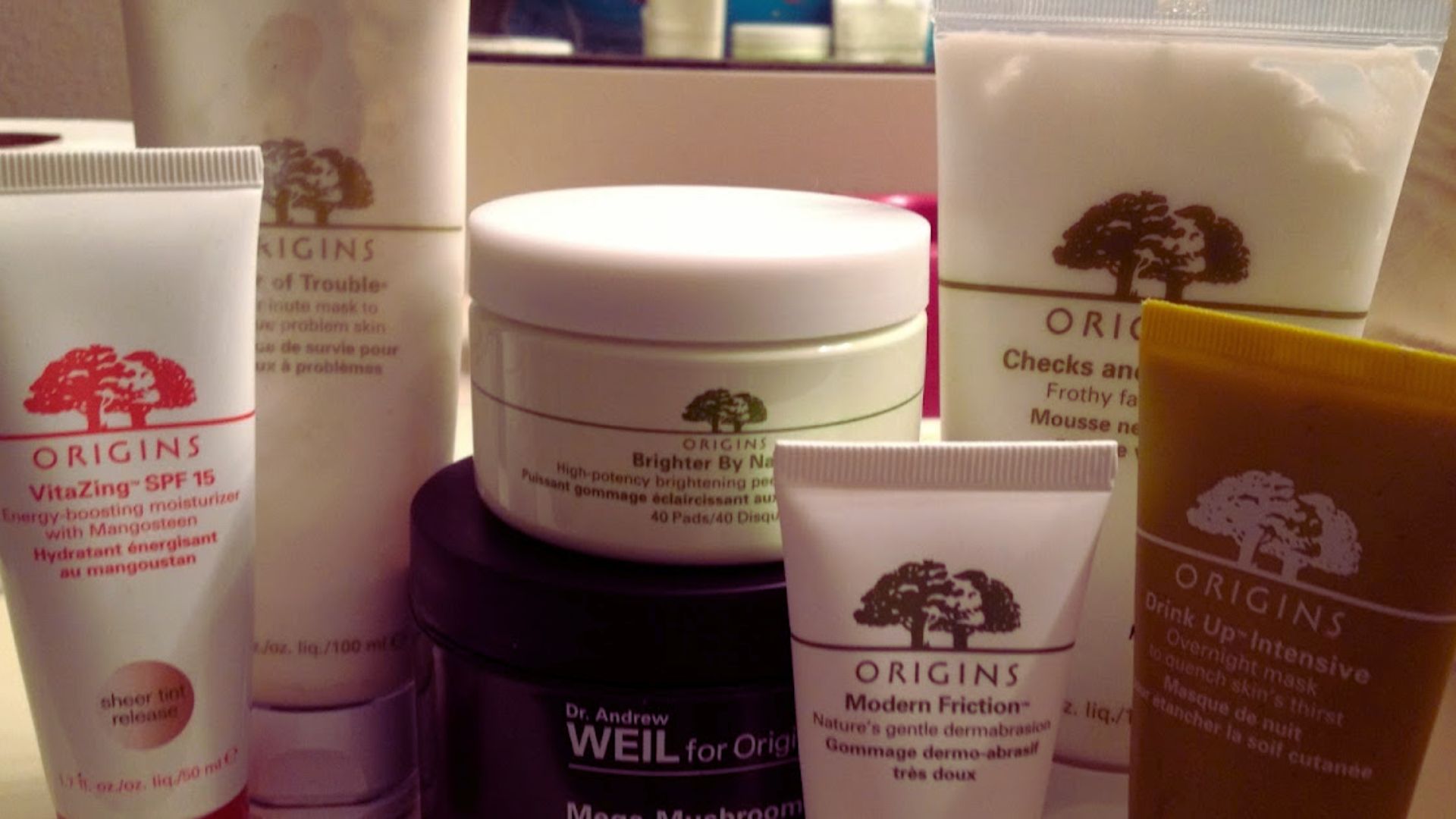 A collection of various Origins skincare products, including moisturizers and scrubs, arranged on a reflective surface. Soft lighting creates a calm tone.