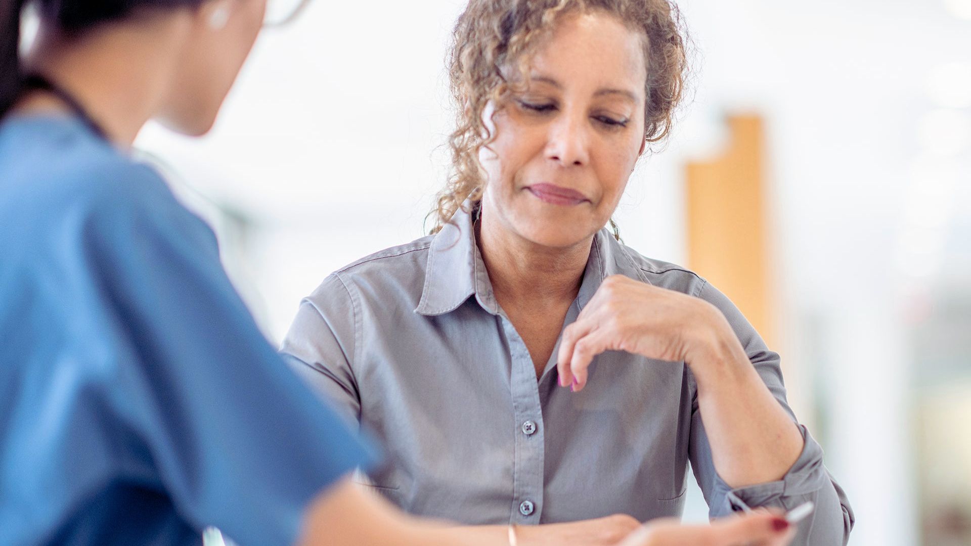 A woman converses with a nurse in a medical setting, discussing health-related concerns.
