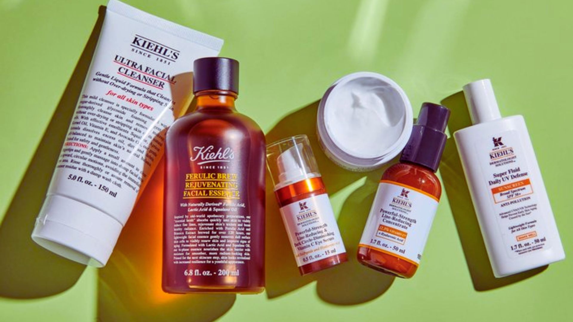 Assorted skincare products on a vibrant green background. Includes bottles and tubes of varying sizes, arranged aesthetically. Bright, fresh vibe.