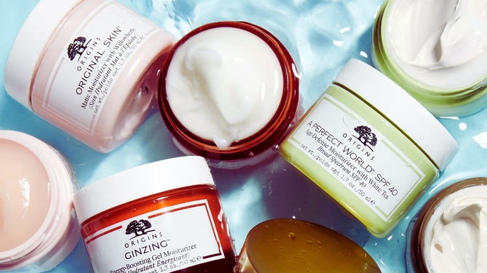 Assorted jars of skincare creams displayed on a reflective, watery surface. Each jar is open, showing creamy textures. The scene feels fresh and luxurious.