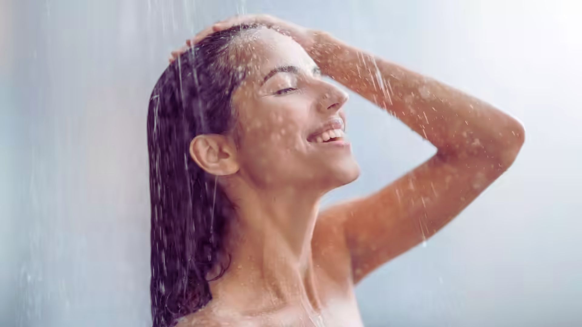A smiling woman enjoying a refreshing shower, with water cascading around her.