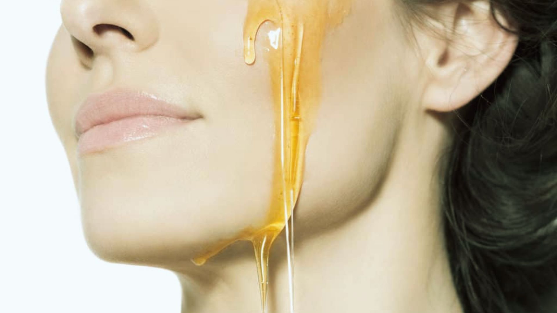 A woman with honey dripping down her face, creating a glossy and textured appearance.