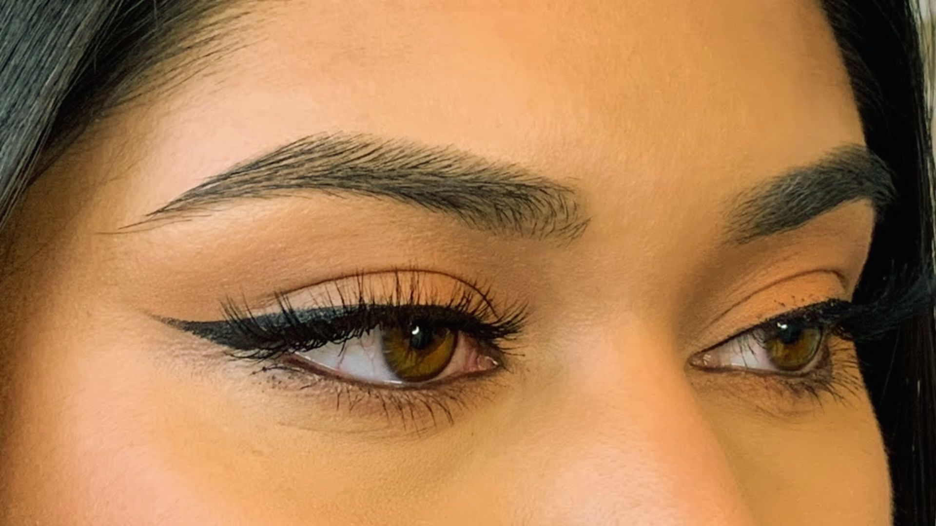 Close-up of a woman's eyes featuring dark brown eyeliner, highlighting her lashes and the shape of her eyes.