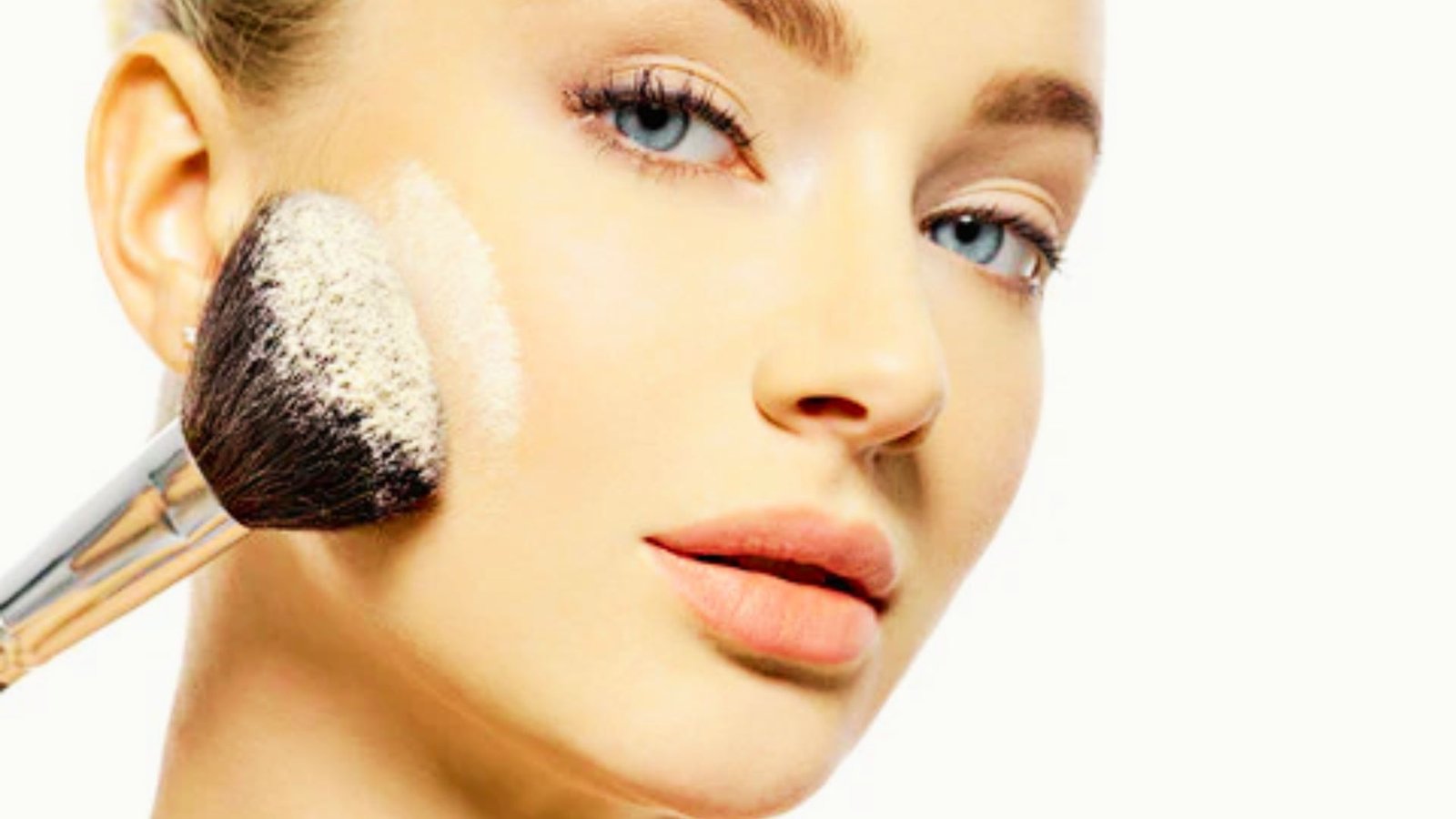 A woman applies makeup to her face using a brush, focusing intently on her reflection in a mirror.