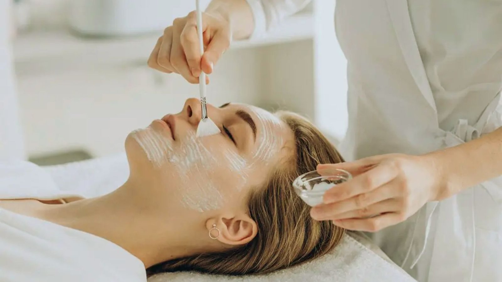 A woman receiving a facial treatment at a serene spa, surrounded by calming decor and soft lighting.