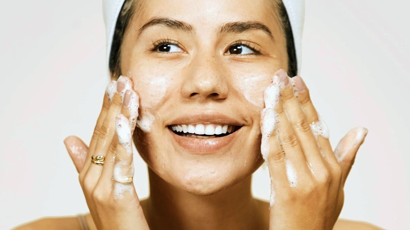 A woman smiles while applying a facial scrub, enjoying her skincare routine.
