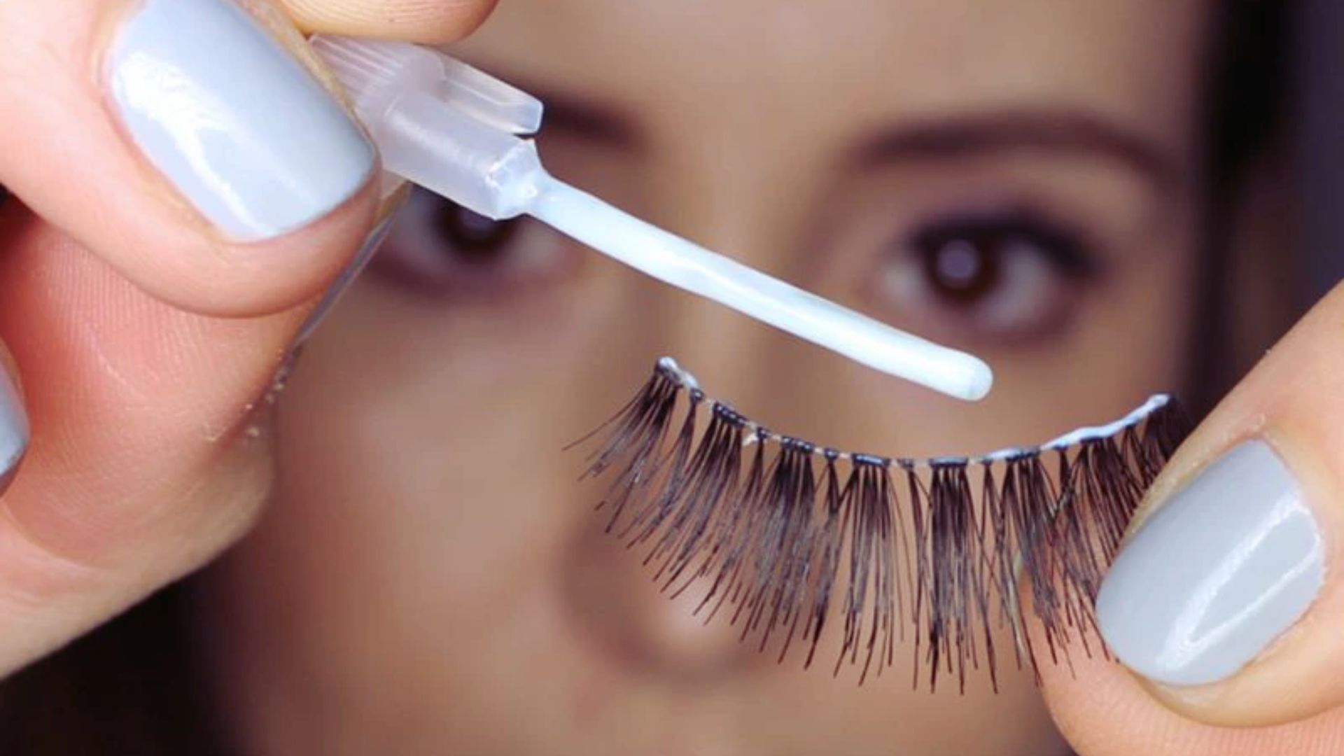 A woman applies mascara to her eyelashes, enhancing her eyes with a focused expression in a well-lit setting.
