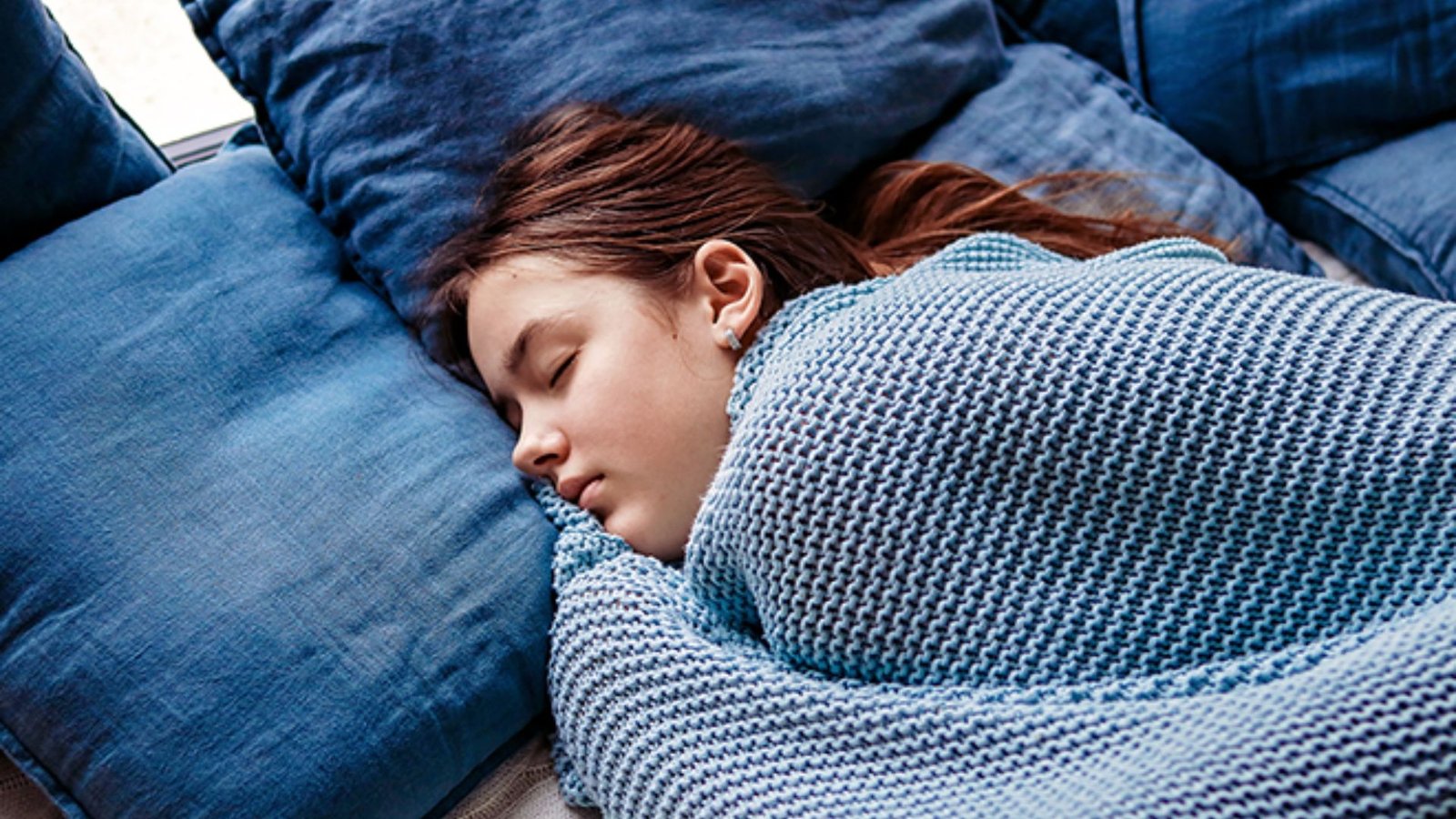 A young girl peacefully sleeping on a couch, wrapped in a cozy blanket.