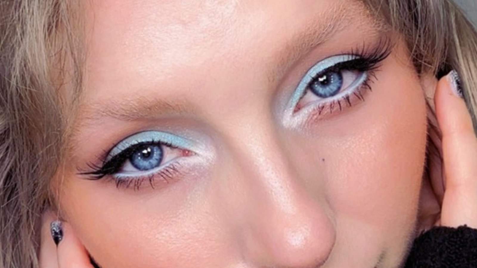 A woman with blue eyes and long black hair, looking directly at the camera with a neutral expression.