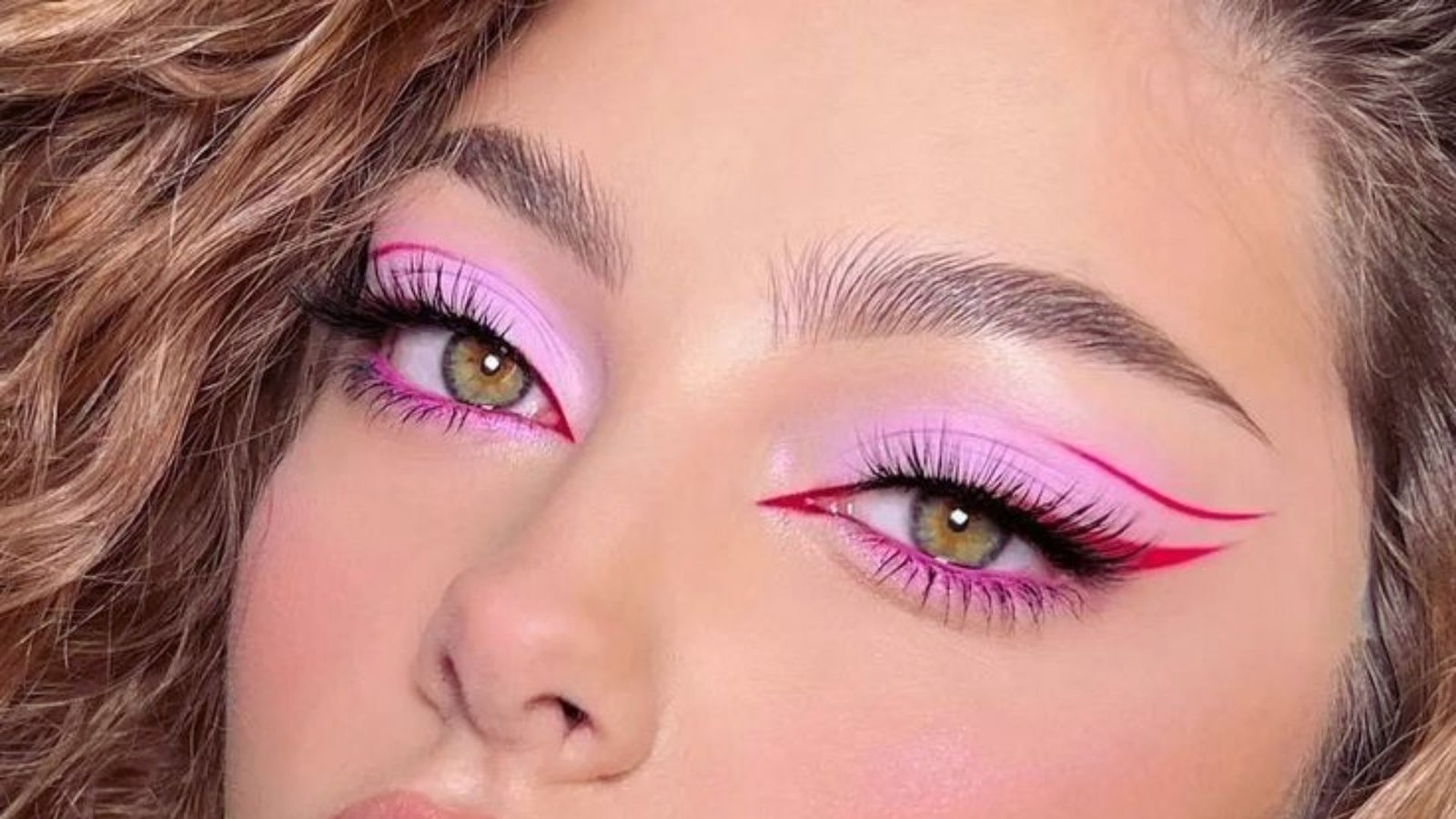 A woman showcasing vibrant pink and purple makeup, highlighting her artistic and bold style.