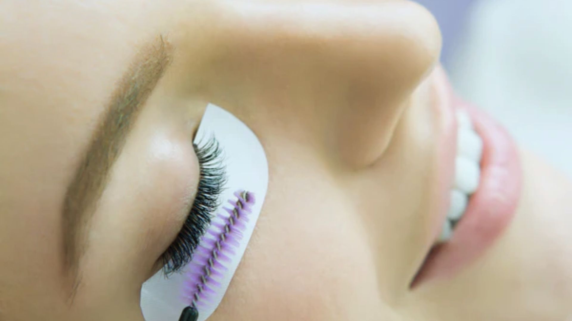 A woman with long eyelashes holds a makeup brush, preparing to apply cosmetics.