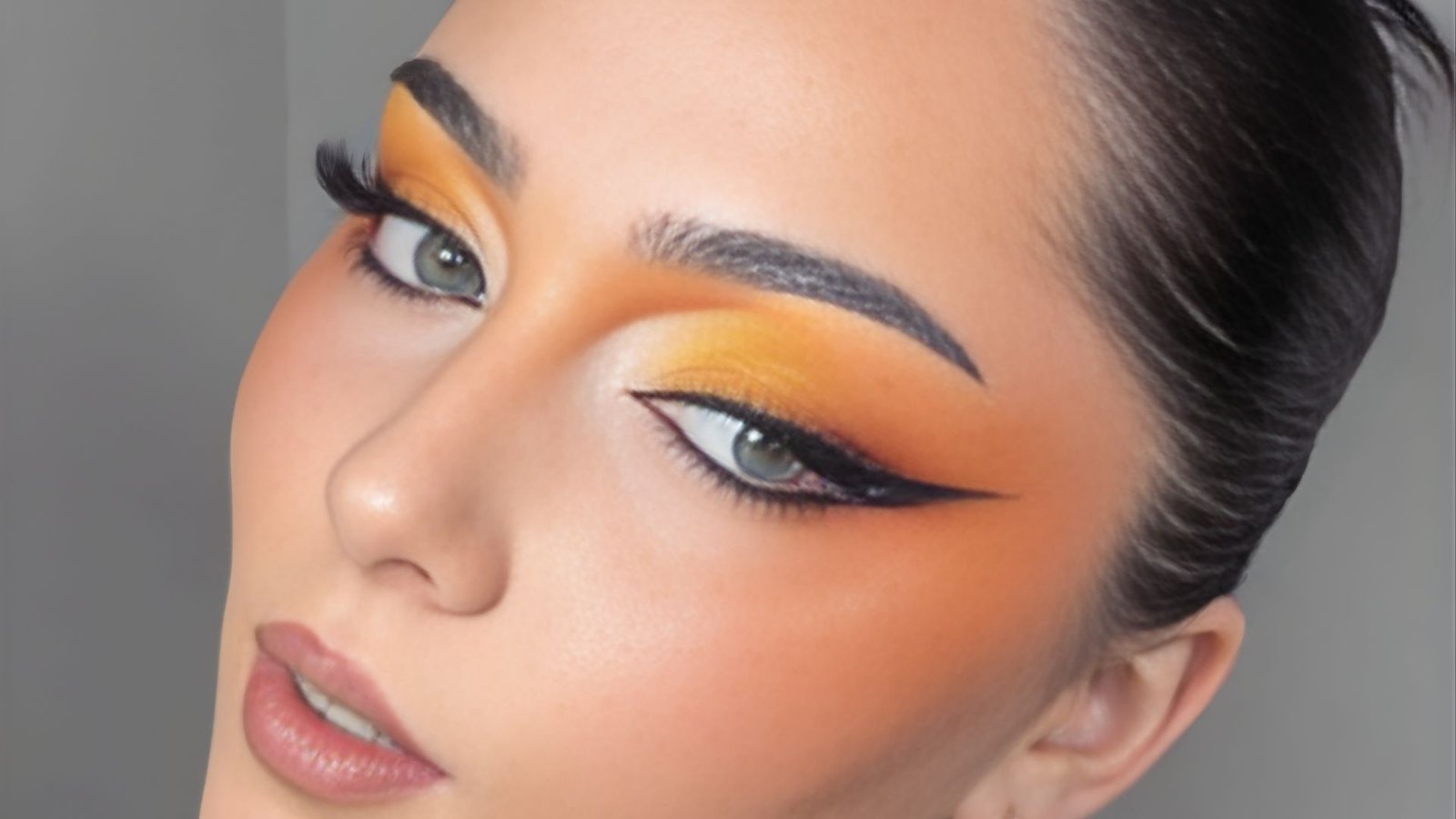 A woman showcasing striking orange and black makeup, highlighting her artistic expression and bold style.