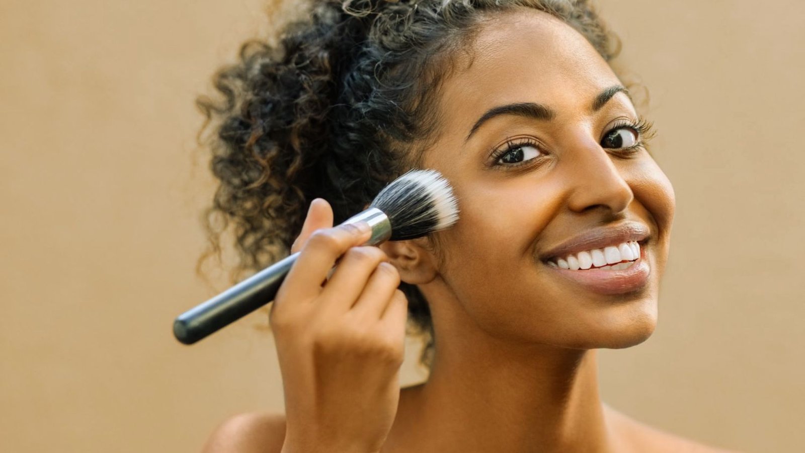 A smiling woman holds a brush, ready to paint or style her hair, exuding creativity and enthusiasm.