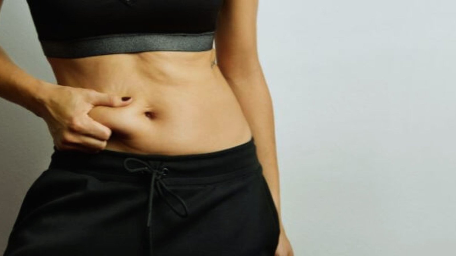 A woman proudly displays her toned abs, showcasing her fitness and strength in a confident pose.
