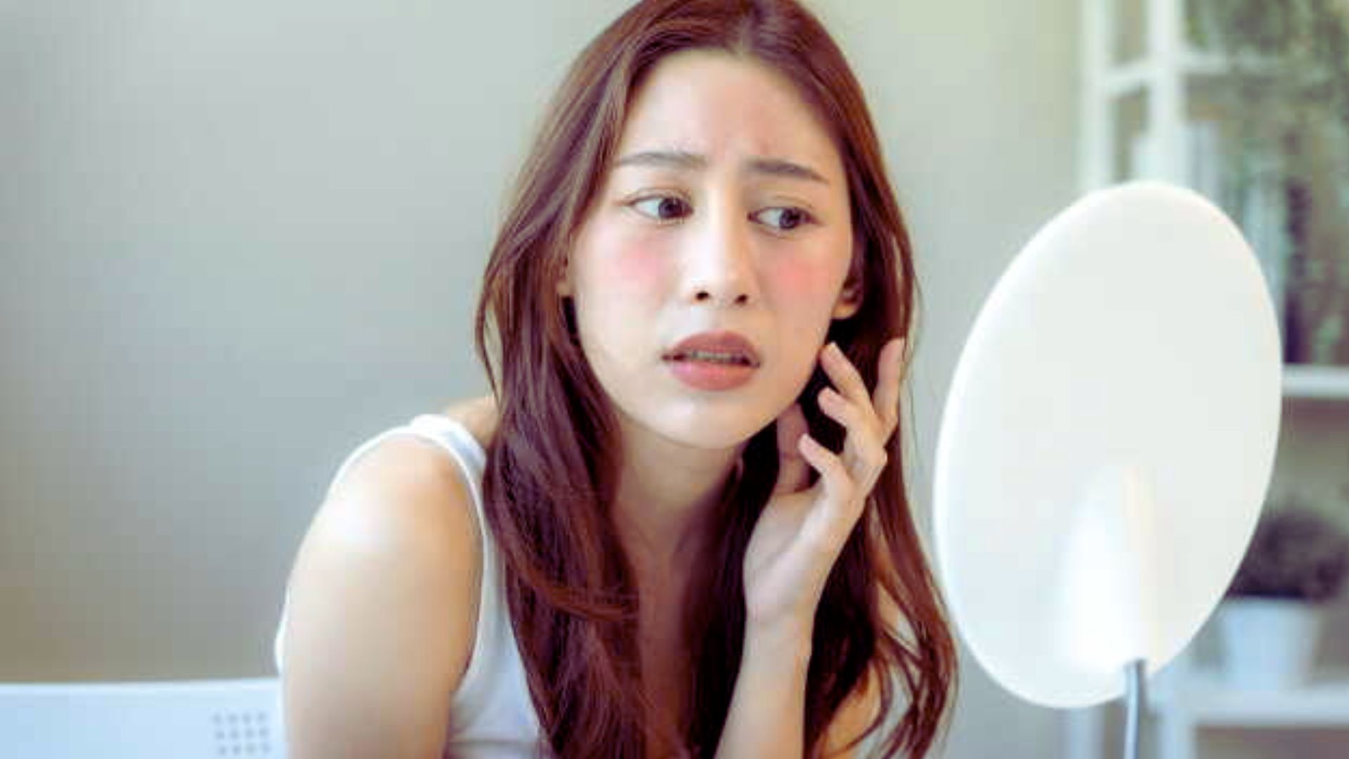 A woman gazes thoughtfully at her reflection in a mirror, contemplating her appearance.
