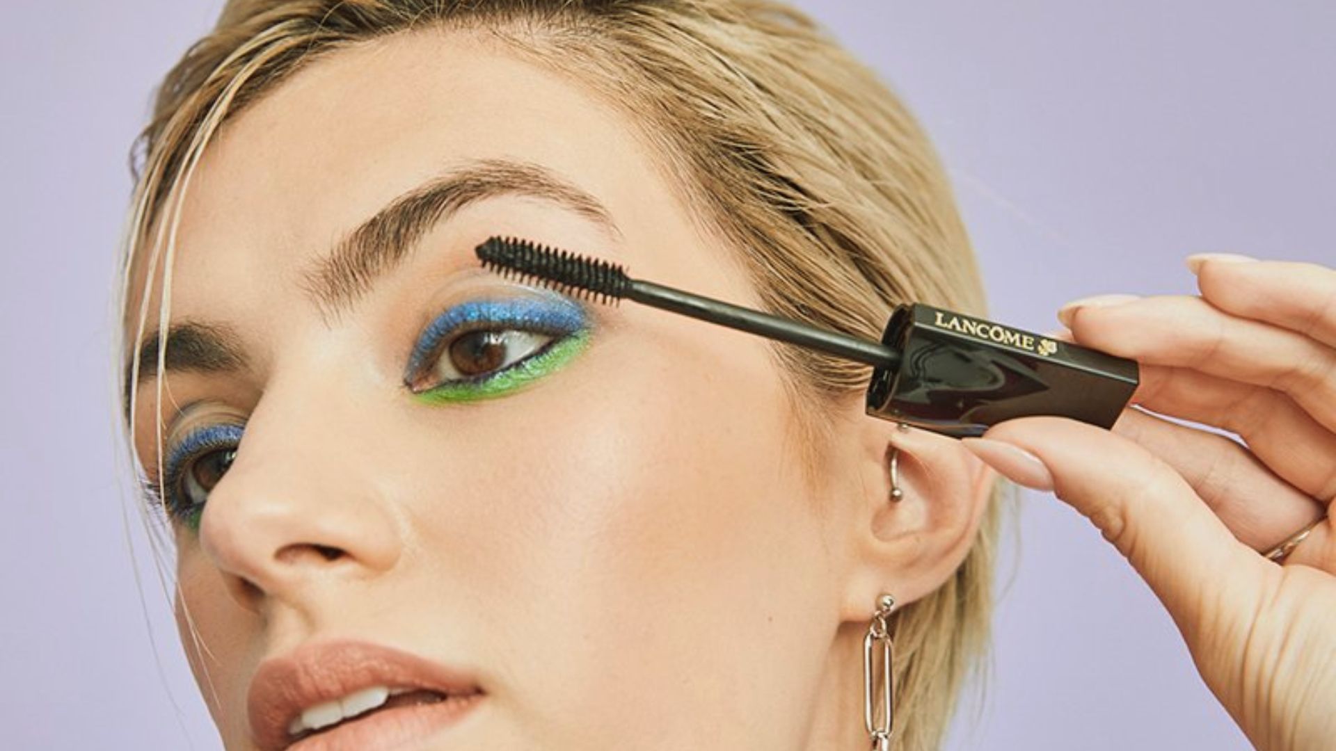 A woman applies mascara to her eyelashes using a brush, focusing intently on her makeup application.