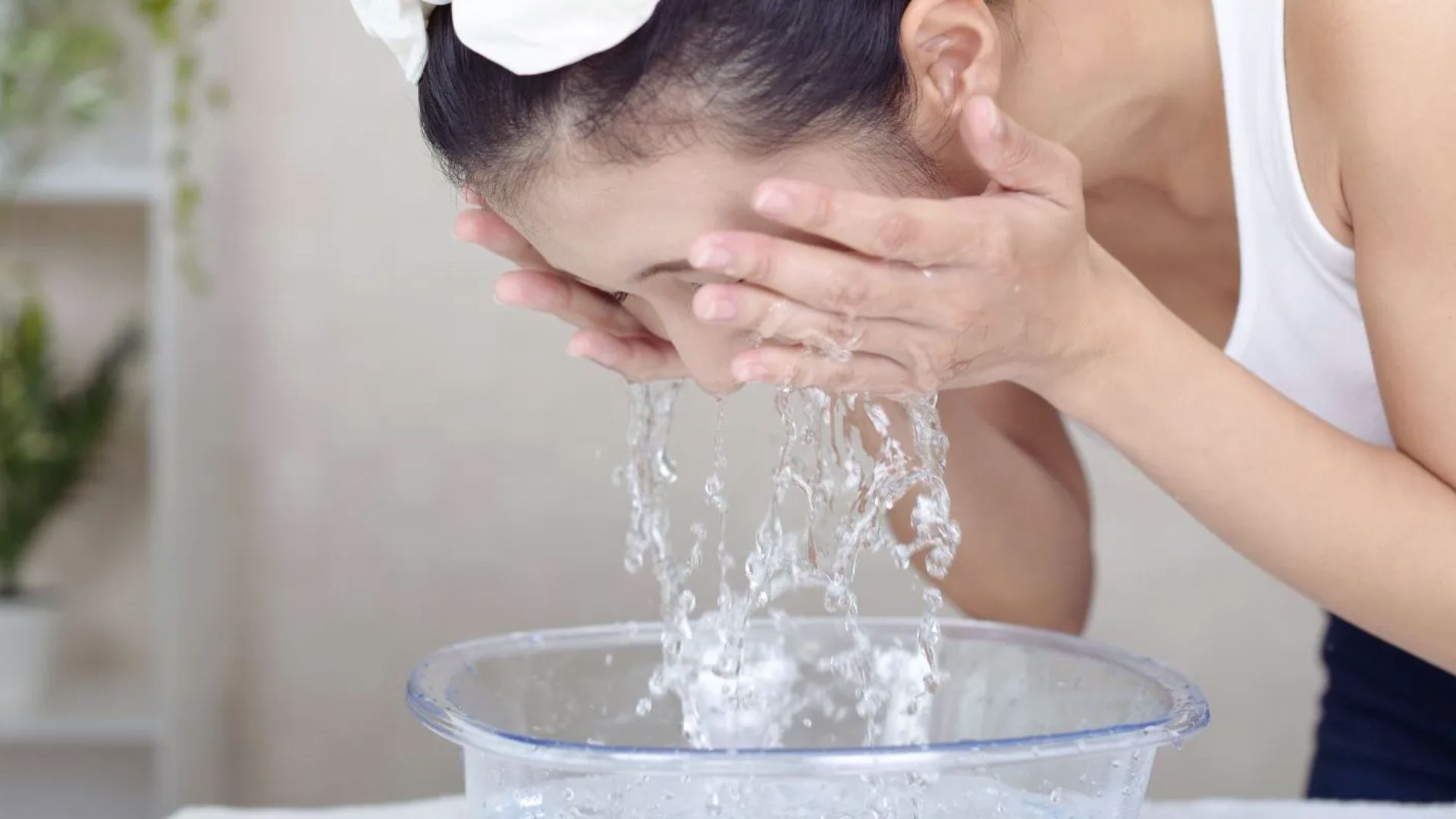 A woman gently washes her face with water, focusing on her skincare routine in a bright bathroom setting.