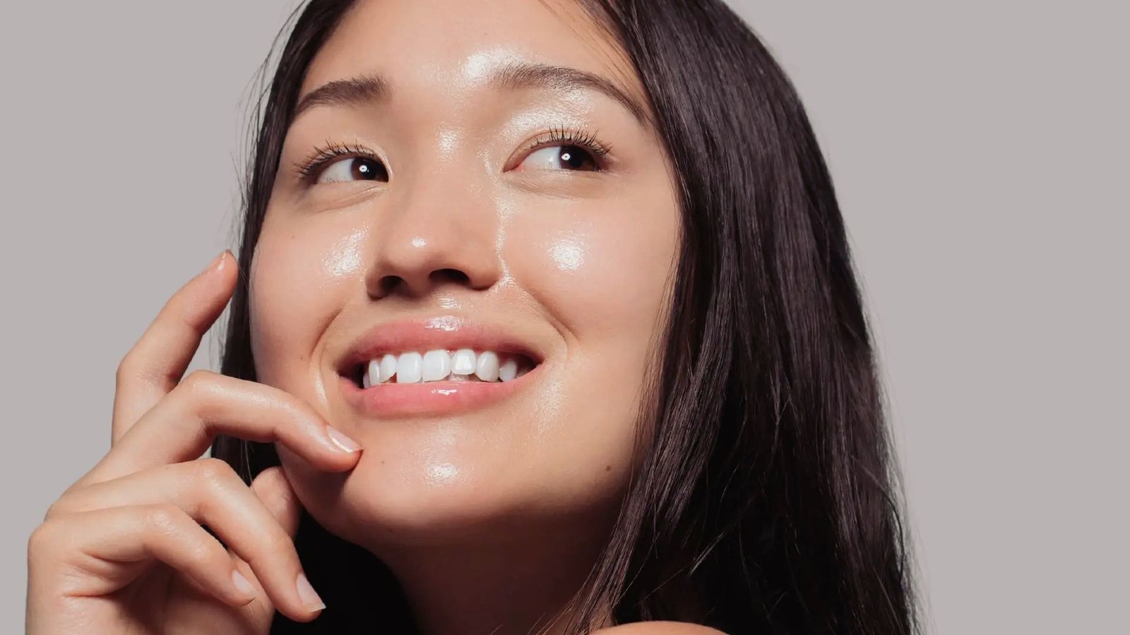 A woman smiles warmly while gently resting her hand on her face, conveying a sense of joy and contentment.