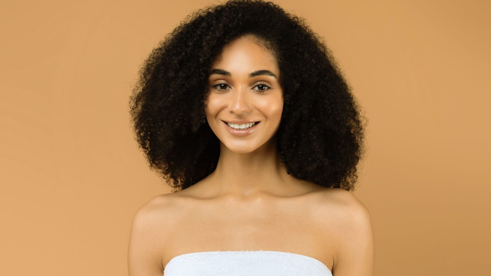 A woman with curly hair wrapped in a towel, looking relaxed and content.