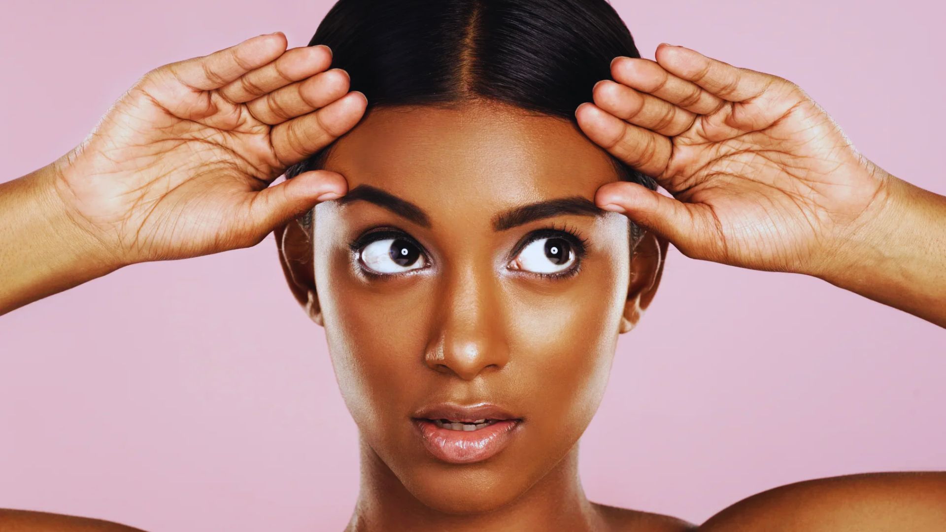A woman stands with her hands on her head, expressing surprise or contemplation.