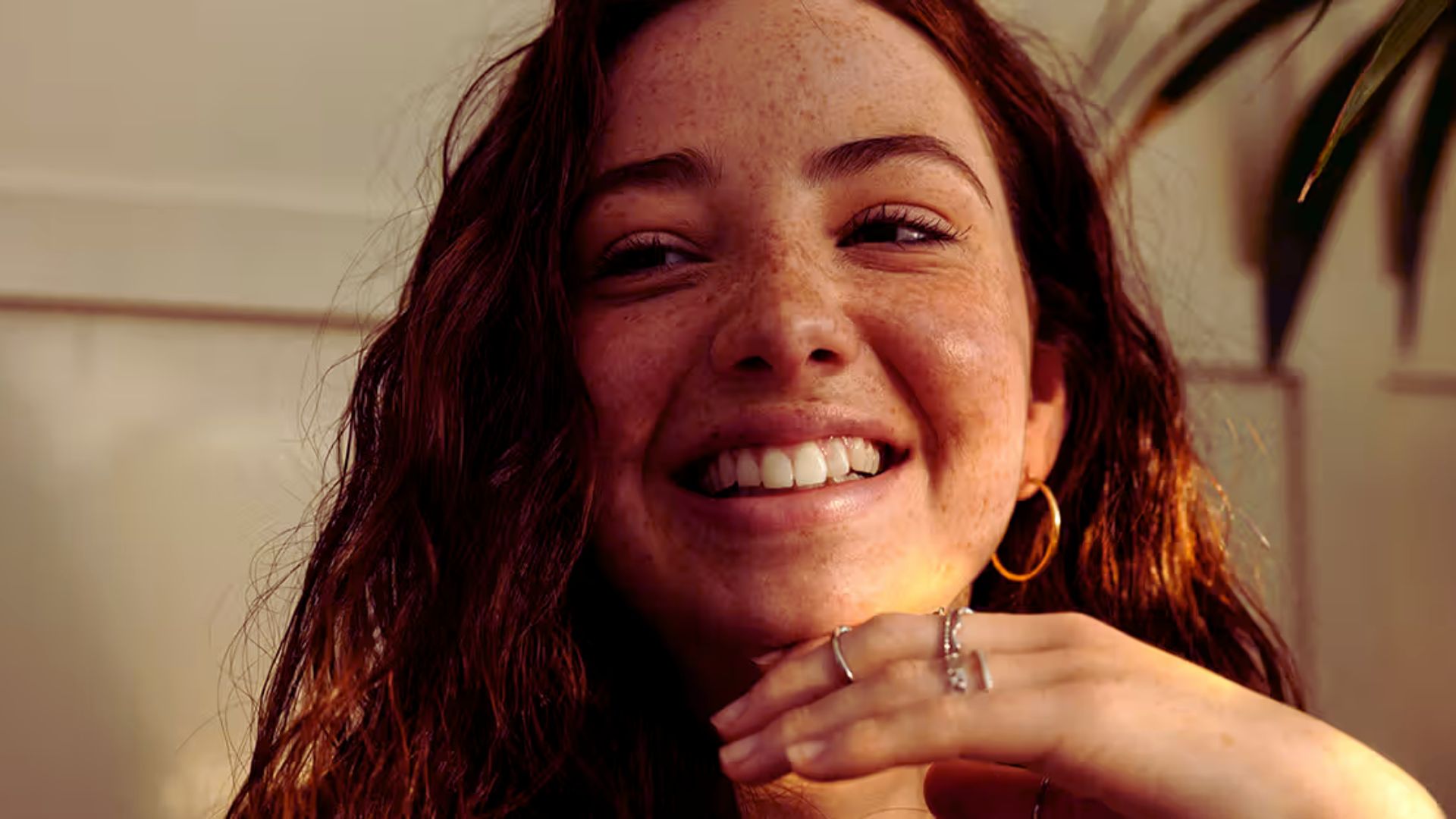 A woman smiling joyfully with her hands gently resting on her face.