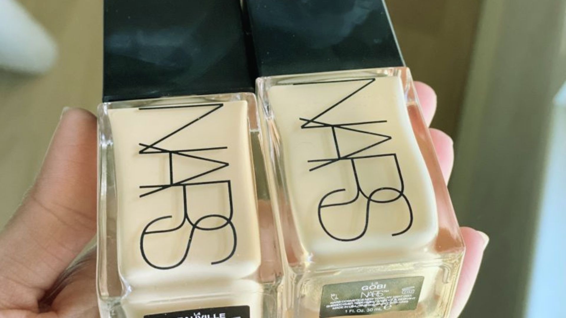 Two bottles of NARS foundation held in a hand, showcasing the product's sleek design and branding.