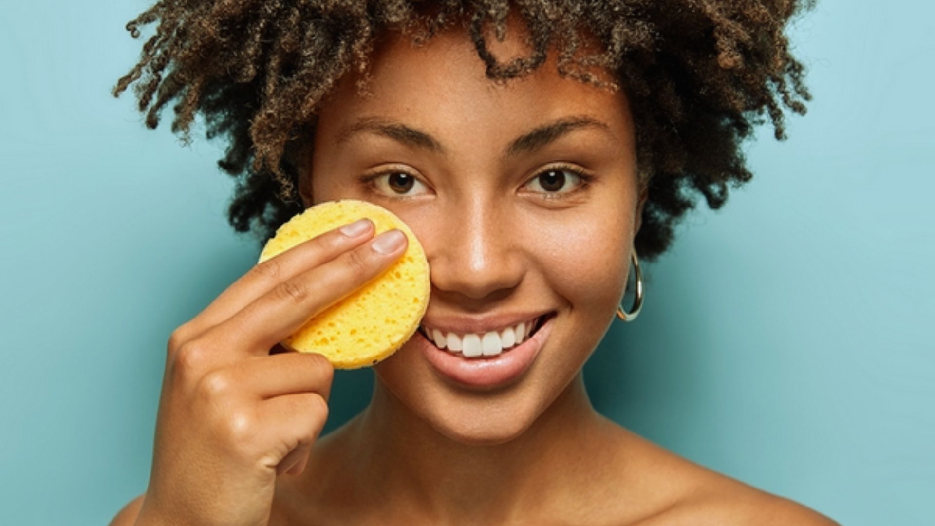 A woman with curly hair holds a sponge, preparing to clean or apply a product.