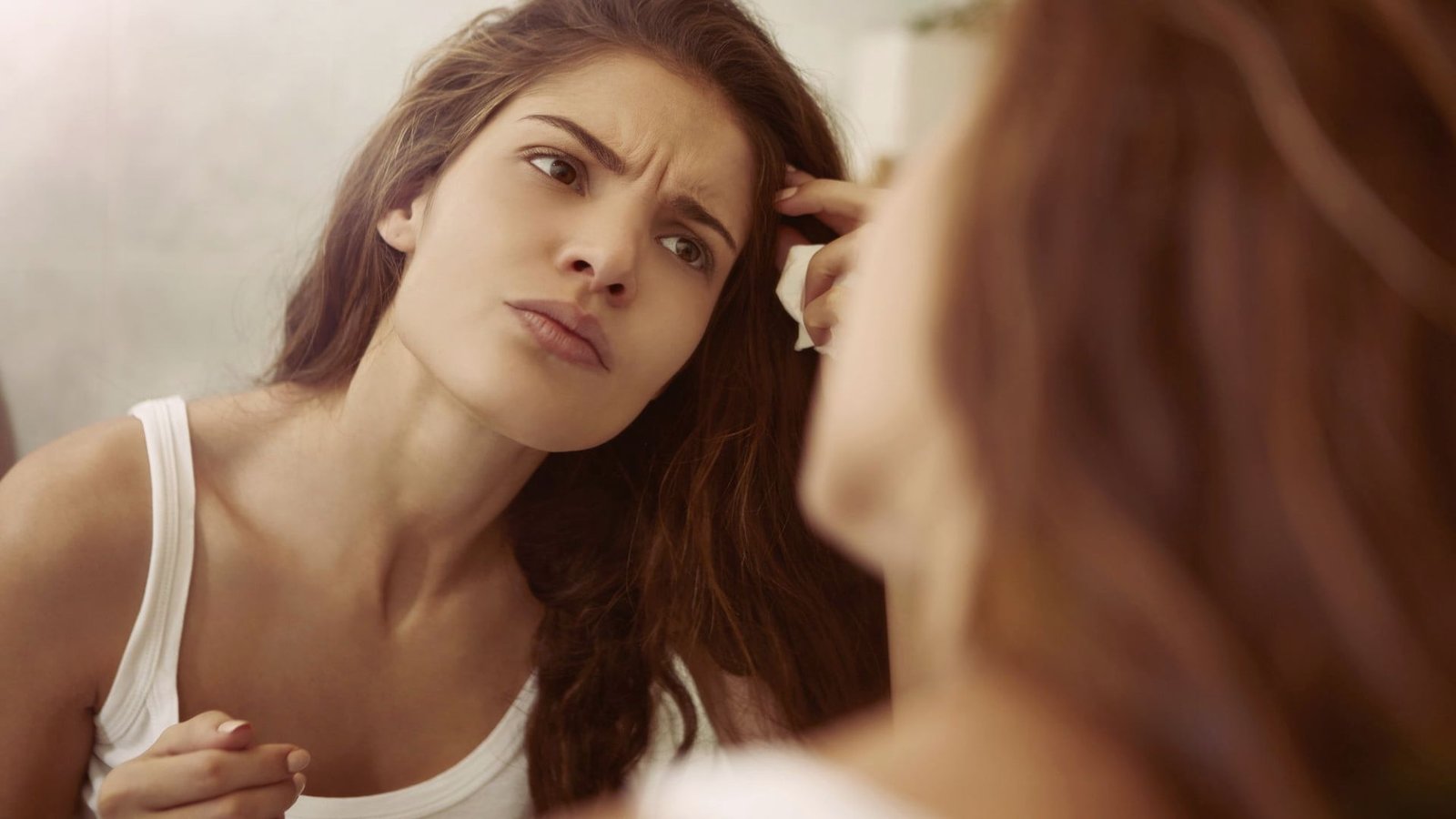A woman combs her hair while gazing into a mirror, reflecting a moment of personal grooming and self-care.