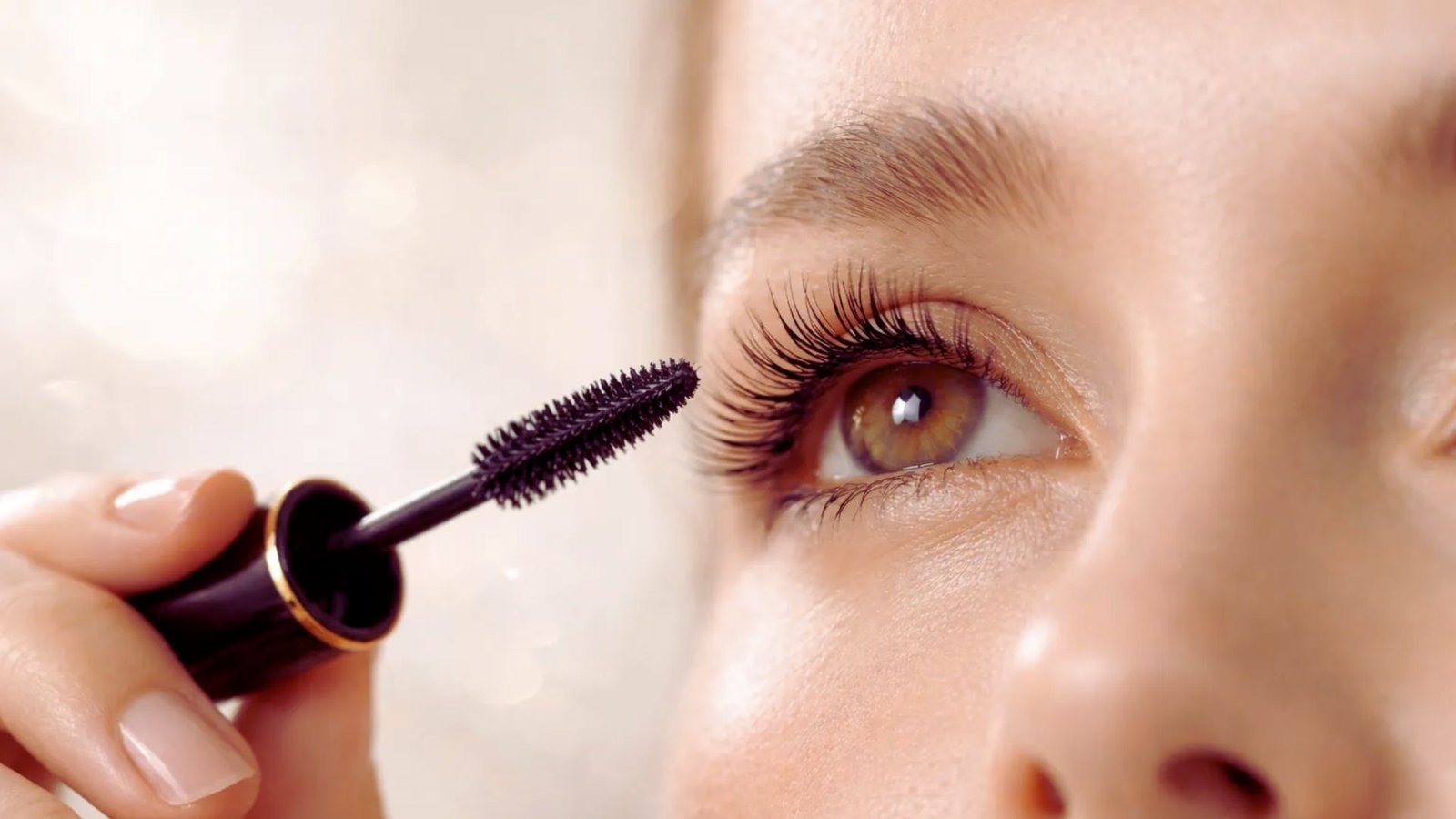 A woman carefully applies mascara to her eyelashes, enhancing her eye makeup with focused attention.